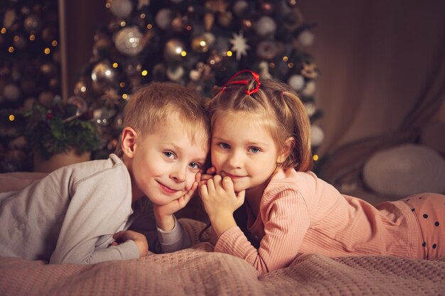 Les enfants sont allongés dans leur lit et regardent la caméra. Décorations de Noël, en attendant les vacances.