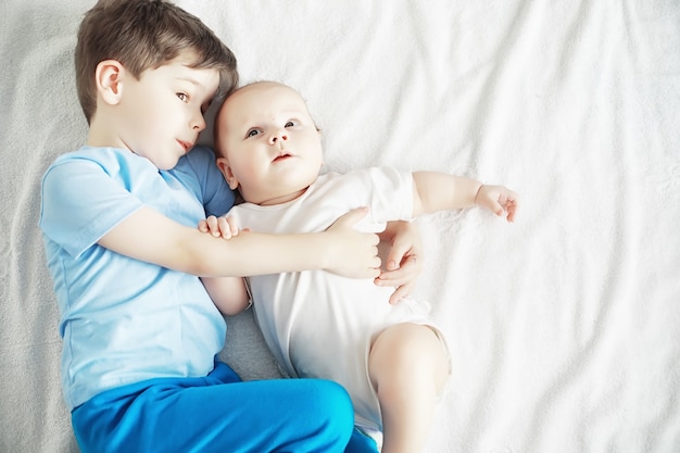 Les enfants sont allongés sur le lit à côté du nouveau-né, petite sœur. Les émotions des enfants.