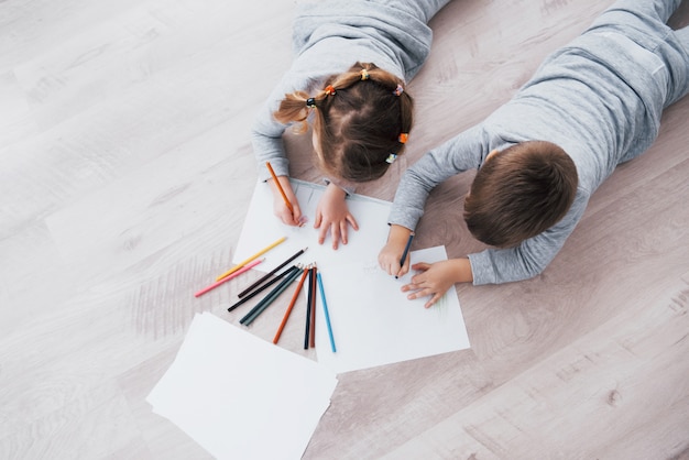 Les enfants sont allongés par terre en pyjama et dessinent avec des crayons. Enfant mignonne peignant avec des crayons