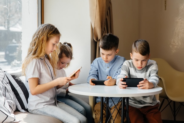 Les enfants sont assis à une table dans un café et jouent ensemble aux téléphones portables. Divertissement moderne.