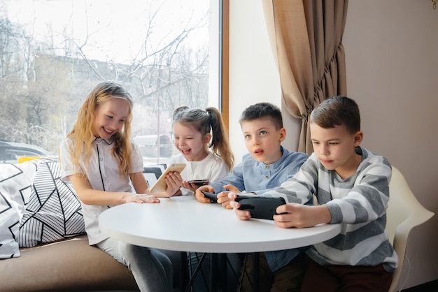 Les enfants sont assis à une table dans un café et jouent ensemble aux téléphones portables. Divertissement moderne.