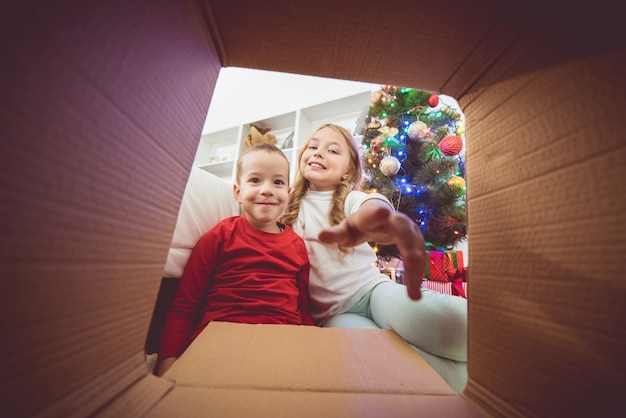 Les enfants souriants ouvrent la boîte près du sapin de Noël