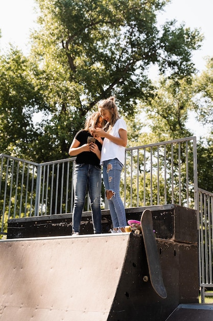 Les enfants sportifs accros au téléphone avec des planches à roulettes et des penny utilisent des téléphones au lieu de patiner et de jouer ensemble Des enfants regardent des smartphones sur une rampe de sport La dépendance des enfants aux téléphones