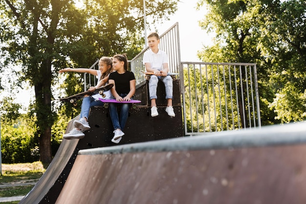 Les enfants sportifs avec des planches à roulettes et des penny sont assis et discutent entre eux sur une rampe de sport sur l'aire de jeux Communication et amitié pour les enfants Mode de vie extrême sportif