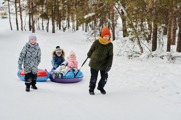 Des enfants tirant des tubes de neige dans la forêt
