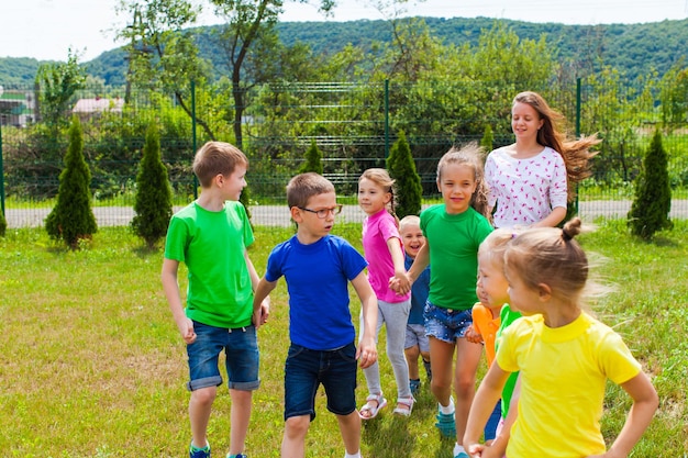 Les enfants avec tuteur vont à l'aire de jeux. Camp d'été, repos à l'extérieur, pelouse verte