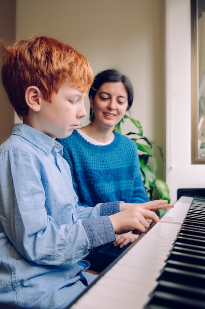 Enfants avec vertu musicale et curiosité artistique. Activités musicales éducatives. Professeur de piano femme enseignant un petit garçon à la maison des leçons de piano. Mode de vie familial passer du temps ensemble à l'intérieur.
