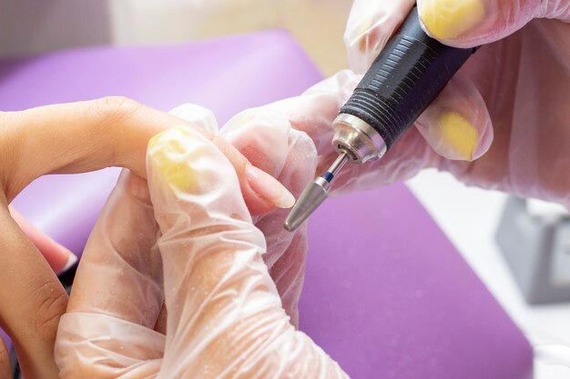 Enlever la gomme laque. manucure matérielle. la manucure fait le polissage de la plaque à ongles au client avec un appareil de manucure