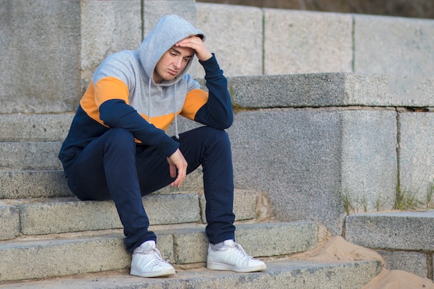 Ennuyé beau mec solitaire assis dans les escaliers et tenant sa tête avec la main. Frustré yound triste homme bouleversé.