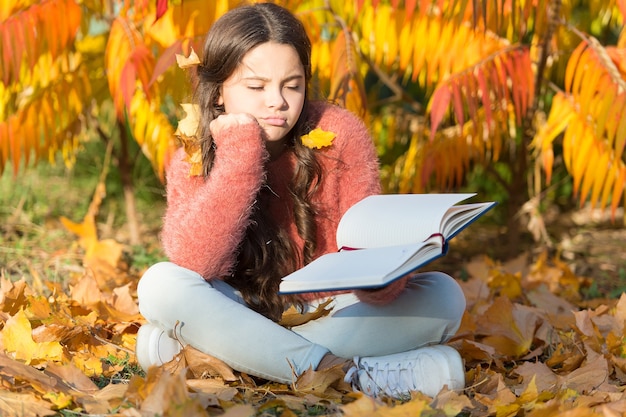 Ennuyé et fatigué. Le petit enfant aime apprendre dans la cour ou dans le parc. Kid étude avec livre. Concept d'auto-éducation. L'enfant aime lire. Étude d'écolière. Étudie chaque jour. Fille lire livre jour d'automne.