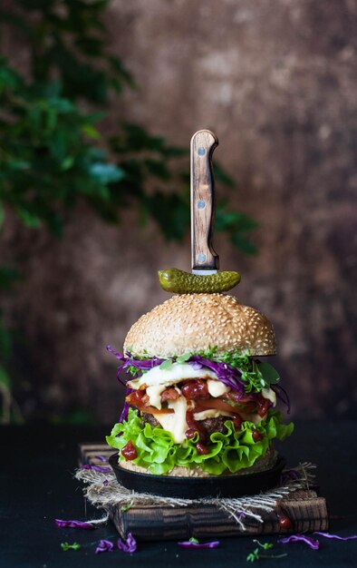 Photo une énorme tour de burger avec une escalope bacon oeuf crème fromage oignons tomates concombres sauce et salade gros plan verticalement style rustique