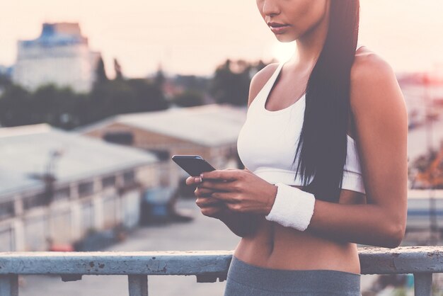 Enregistrer ses résultats. Gros plan de la belle jeune femme en vêtements de sport tenant un téléphone intelligent