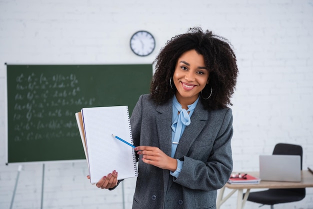 Un enseignant afro-américain souriant pointant du doigt un cahier dans la salle de classe.