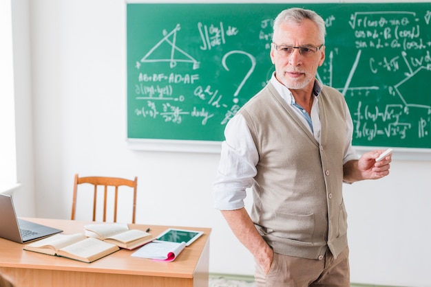 Photo enseignant âgé avec une craie expliquant les mathématiques