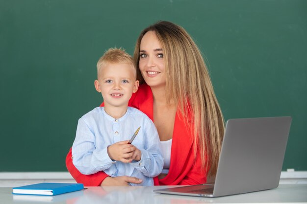 Enseignant aidant un écolier en classe à l'école mère et fils ensemble à l'aide d'un ordinateur portable à l'école