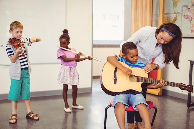 Photo enseignant aidant un enfant à jouer d'un instrument de musique en classe