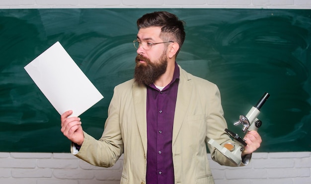 Un enseignant barbu tient des documents et un fond de tableau au microscope La biologie est sa passion Enseignant exigeant Maître de conférences en classe Expliquer la théorie Collège et lycée Se préparer au test