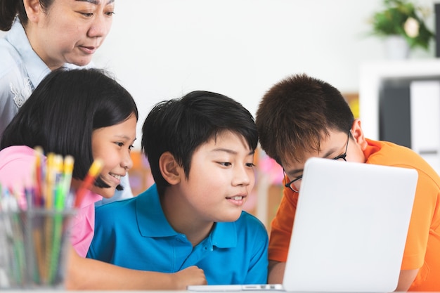 Enseignant et enfants asiatiques mignons utilisant l&#39;ordinateur portable ensemble.