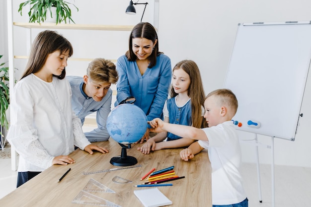 L'enseignant et les enfants de la classe regardent le globe, l'enseignant aide à expliquer la leçon aux enfants de la classe à un bureau