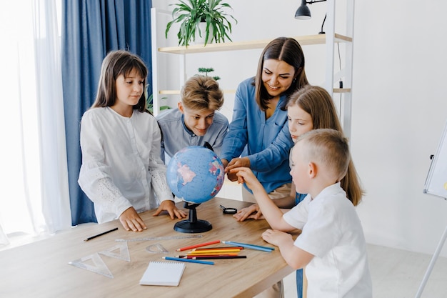 L'enseignant et les enfants de la classe regardent le globe, l'enseignant aide à expliquer la leçon aux enfants de la classe à un bureau