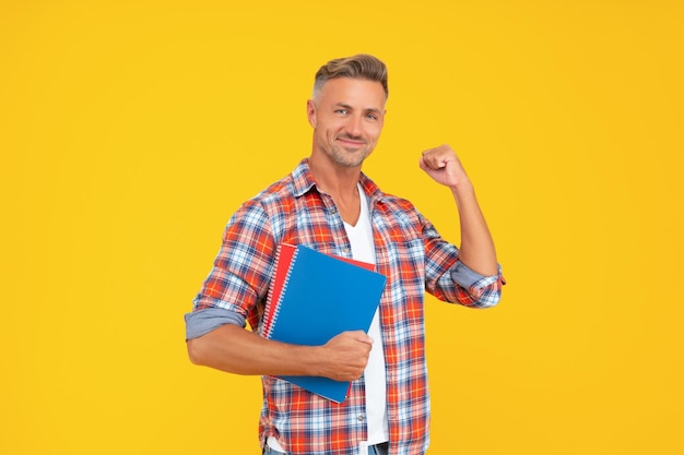 Enseignant de gars excité faisant un geste gagnant tenant des livres éducation de fond jaune