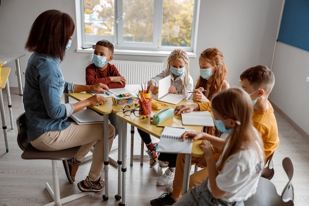 Enseignant en masque expliquant aux écoliers pendant une leçon à l'école