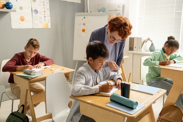 Enseignant penché sur le bureau de l'écolier pendant le travail individuel