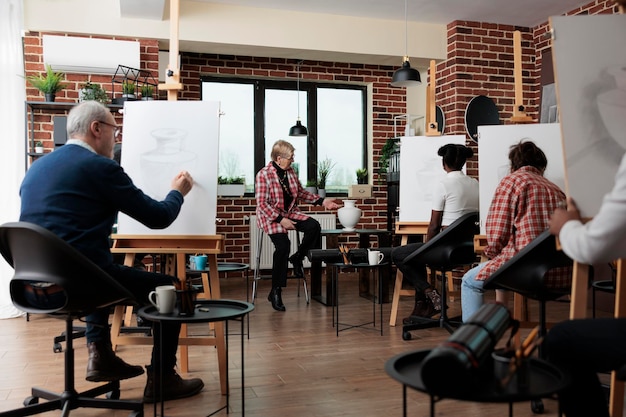 Enseignant principal expliquant la technique de dessin aux étudiants en art multiethnique lors d'un atelier créatif. Équipe diversifiée apprenant à dessiner un modèle sur toile à l'aide d'un crayon graphique. Les résolutions du nouvel an