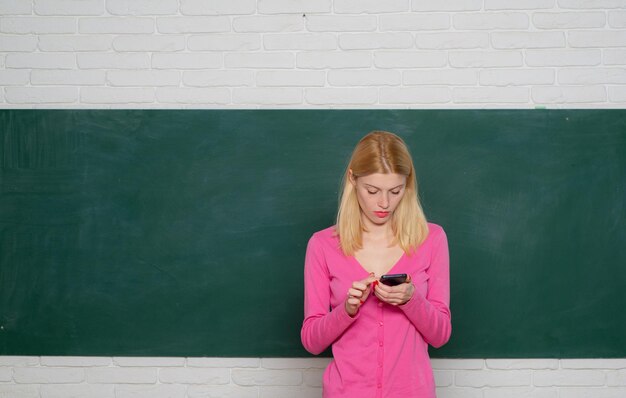 L'enseignant avec un téléphone portable dans la salle de classe sur fond de tableau noir. Concept d'enseignement et d'apprentissage des personnes.