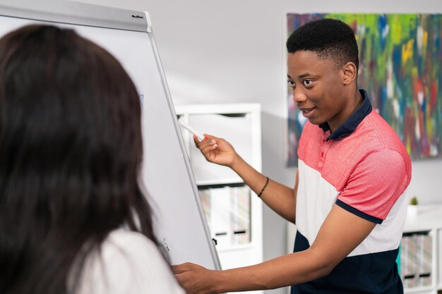 L'enseignant tient une tablette dans les mains se tient au tableau noir avec un jeune beau garçon étudiant tient un marqueur