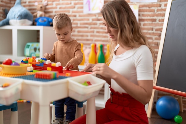 Enseignant et tout-petit jouant avec des blocs de construction assis sur une table à la maternelle