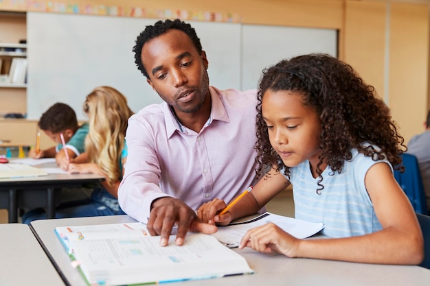 Photo enseignant travaillant avec une fille de l'école primaire à son bureau