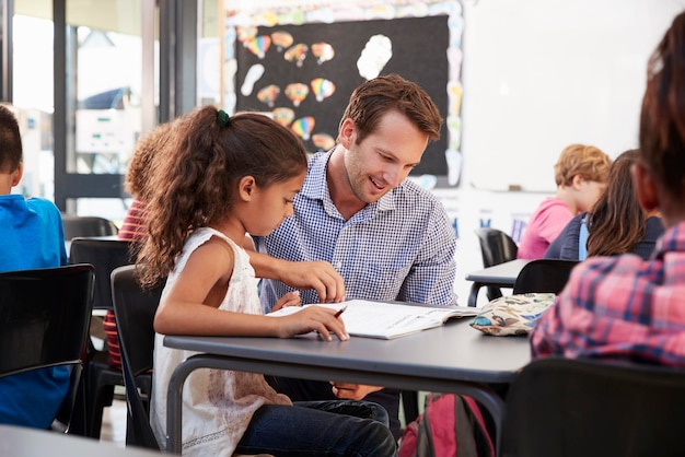 Enseignant travaillant avec une jeune écolière à son bureau en classe