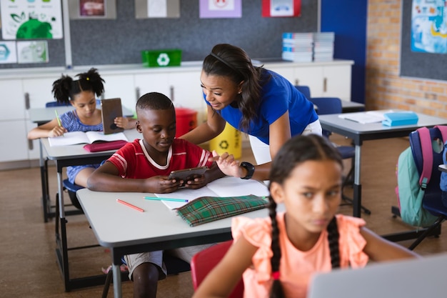 Une enseignante afro-américaine apprend à un garçon à utiliser une tablette numérique en classe à l'école primaire