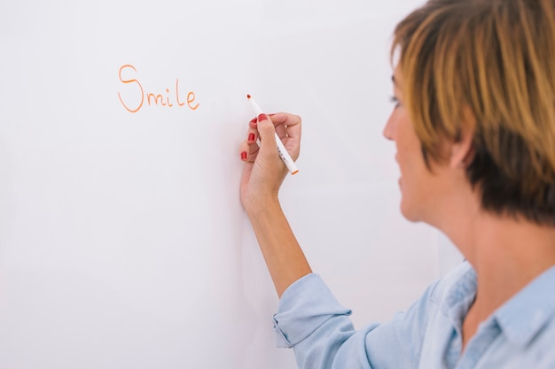 Enseignante écrit sur un tableau blanc le mot sourire.