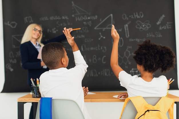 Une enseignante enseigne aux écoliers au tableau noir dans la salle de classe Équipe internationale Retour à l'école