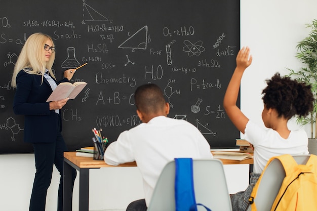 Une enseignante enseigne aux écoliers au tableau noir dans la salle de classe Équipe internationale Retour à l'école