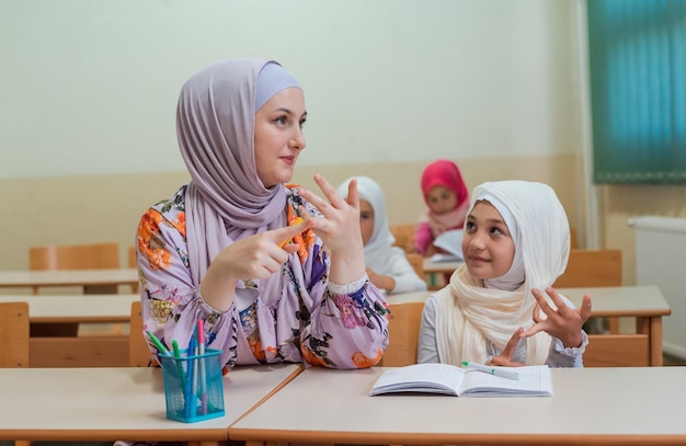 Une enseignante musulmane en hijab aide un écolier à apprendre à compter pendant le cours en classe.