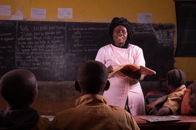 Une enseignante noire se tient devant explique la leçon en lisant le livre du bureau