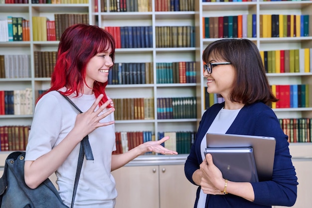 Enseignante parlant à une étudiante adolescente à l'intérieur de la bibliothèque