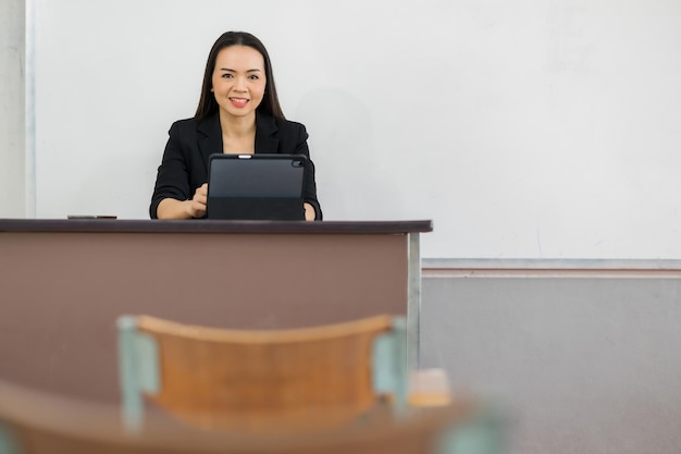 Une enseignante avec une tablette est assise dans une salle de classe vide à l'université. en attendant d'enseigner aux élèves de la classe