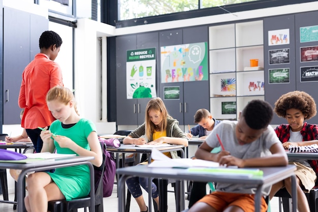 Des enseignantes et des élèves divers assis à des bureaux et écrivant dans l'espace de copie de la salle de classe