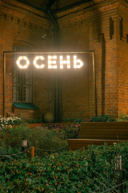 Enseigne au néon dans le parc avec l'inscription Automne en russe, dans la perspective d'un beau mur de briques