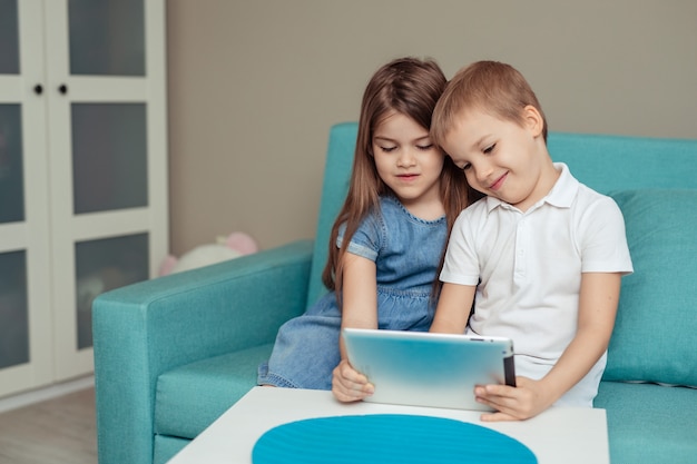 enseignement à distance à domicile. Frères et sœurs jumeaux étudient à la maison à l'aide d'une tablette