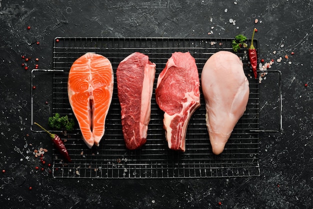 Ensemble d'aliments crus de steaks avec saumon, veau, boeuf et poulet sur fond de pierre sombre Vue de dessus Aliments biologiques