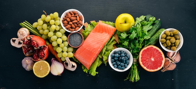 Un ensemble d'aliments sains Poisson noix protéines baies légumes et fruits Sur un fond en bois noir Vue de dessus Espace libre pour le texte