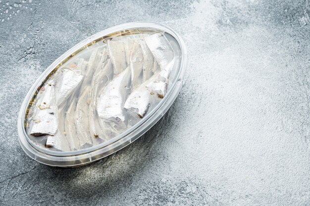 Ensemble d'anchois marinés, dans un récipient en plastique, sur fond gris