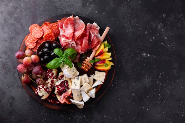 Photo un ensemble d'apéritifs pour le vin, le jamon, le pepperoni, le fromage, les raisins, la pêche et les olives sur une vue de dessus de planche de bois.