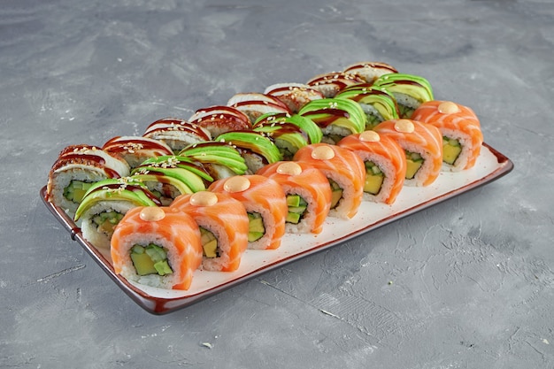 Ensemble appétissant de rouleaux de sushi dragon avec saumon, avocat et anguille dans une assiette blanche sur fond gris