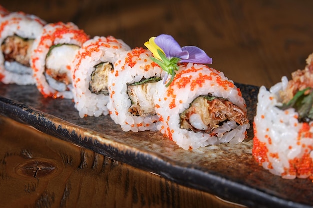 Ensemble d'appétissants tobiko uramaki de cuisine japonaise servis sur une longue assiette avec fleur décorative